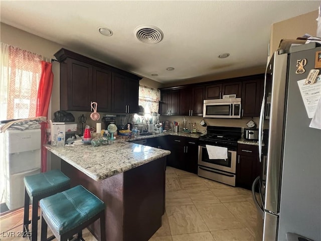 1429 S Sandhill Rd, Las Vegas, NV 89104 - kitchen with stainless steel appliances, a peninsula, dark brown cabinets, a kitchen breakfast bar, and light stone countertops