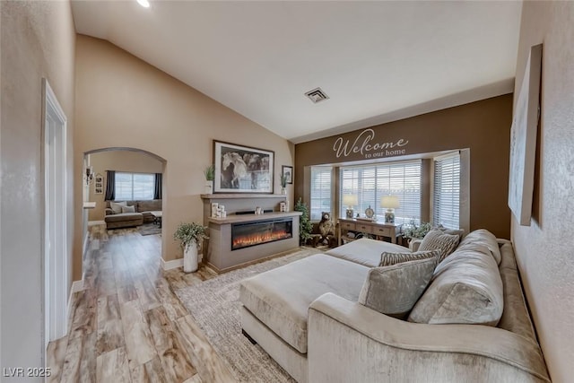 7670 Descanso Ln, Las Vegas, NV 89123 - living room featuring a glass covered fireplace, light wood-style flooring, high vaulted ceiling, and arched walkways