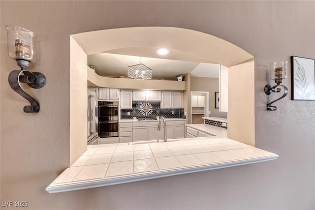 7670 Descanso Ln, Las Vegas, NV 89123 - kitchen with appliances with stainless steel finishes, tile countertops, decorative backsplash, a textured wall, and arched walkways
