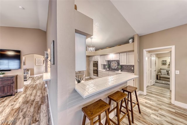7670 Descanso Ln, Las Vegas, NV 89123 - kitchen featuring light wood finished floors, stainless steel appliances, white cabinetry, a breakfast bar, and tile countertops