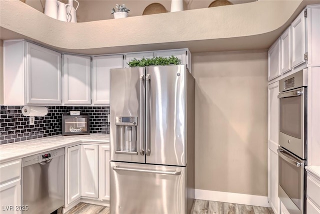 7670 Descanso Ln, Las Vegas, NV 89123 - kitchen with appliances with stainless steel finishes, tile counters, white cabinetry, decorative backsplash, and light wood finished floors