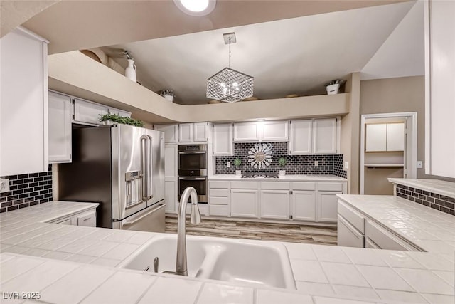 7670 Descanso Ln, Las Vegas, NV 89123 - kitchen with stainless steel appliances, tile counters, backsplash, vaulted ceiling, and white cabinets