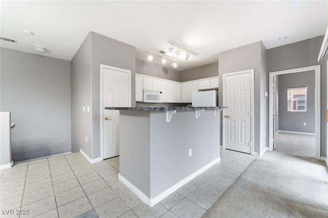 9303 Gilcrease Ave Unit 1013, Las Vegas, NV 89149 - kitchen featuring white microwave, light tile patterned floors, white cabinetry, a breakfast bar, and fridge