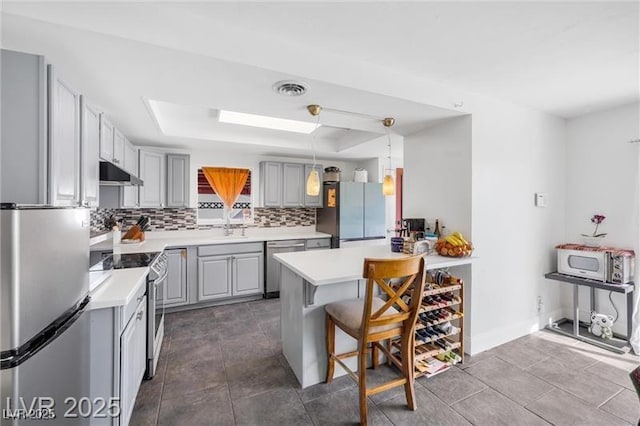 1589 Silver Mesa Way, Las Vegas, NV 89169 - kitchen with stainless steel appliances, under cabinet range hood, a raised ceiling, gray cabinets, and backsplash