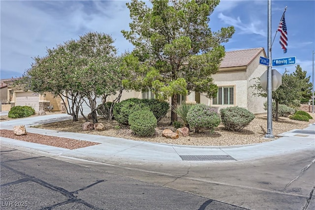 7465 Widewing Dr, North Las Vegas, NV 89084 - view of property hidden behind natural elements featuring stucco siding, driveway, a tile roof, and an attached garage