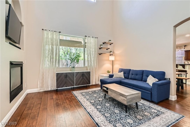 9192 Moose Country Pl, Las Vegas, NV 89178 - living area featuring dark wood-style floors, a towering ceiling, plenty of natural light, baseboards, and arched walkways