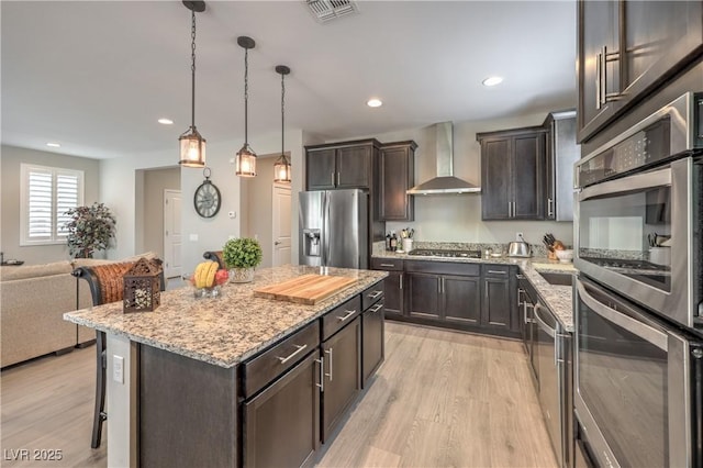 2711 Evolutionary Ln, Las Vegas, NV 89138 - kitchen featuring appliances with stainless steel finishes, wall chimney exhaust hood, light wood finished floors, a kitchen breakfast bar, and recessed lighting