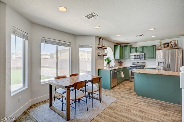 412 Orchid Oasis Ave, North Las Vegas, NV 89031 - kitchen featuring green cabinetry, appliances with stainless steel finishes, open shelves, decorative backsplash, and light wood finished floors