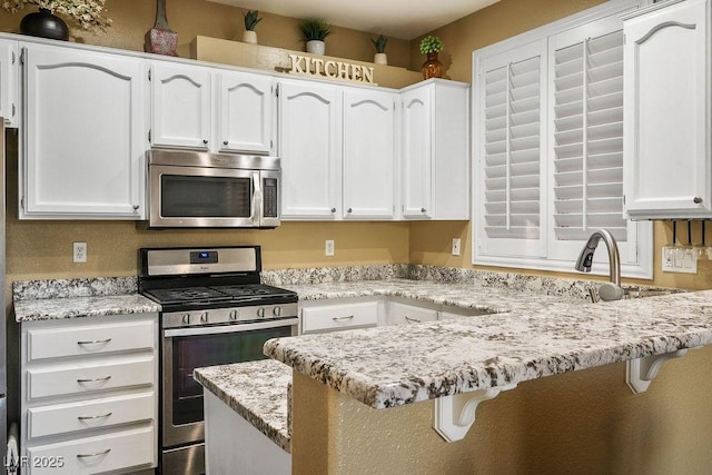 499 Eagle Vista Dr, Henderson, NV 89012 - kitchen featuring appliances with stainless steel finishes, white cabinets, a peninsula, a kitchen bar, and light stone counters