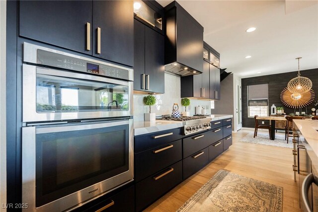 2750 Evolutionary Ln, Las Vegas, NV 89138 - kitchen featuring appliances with stainless steel finishes, light countertops, decorative light fixtures, wall chimney exhaust hood, and light wood-style flooring