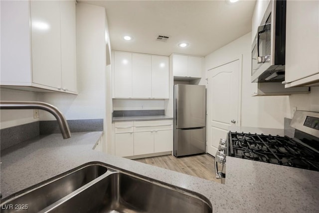 7400 W Flamingo Rd Unit 1082, Las Vegas, NV 89147 - kitchen featuring appliances with stainless steel finishes, white cabinetry, recessed lighting, light stone countertops, and light wood finished floors
