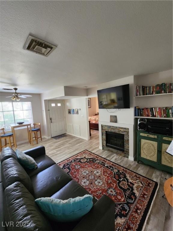 4805 S Torrey Pines Dr Unit 101, Las Vegas, NV 89103 - living room with wood finished floors, a textured ceiling, a fireplace, a ceiling fan, and baseboards