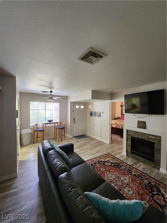 4805 S Torrey Pines Dr Unit 101, Las Vegas, NV 89103 - living room featuring wood finished floors, a ceiling fan, a textured ceiling, a stone fireplace, and baseboards