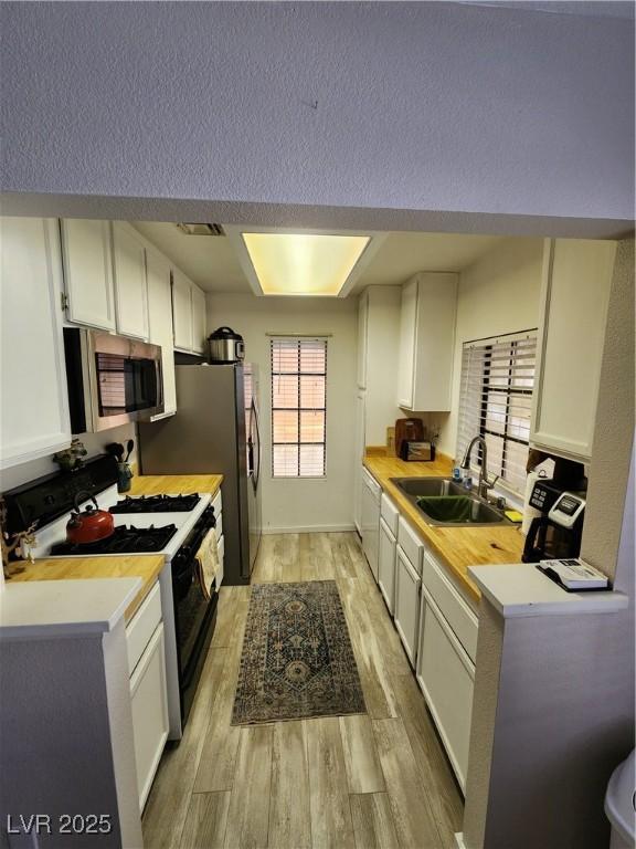 4805 S Torrey Pines Dr Unit 101, Las Vegas, NV 89103 - kitchen featuring stainless steel microwave, gas range, a sink, white cabinetry, and light wood-style flooring