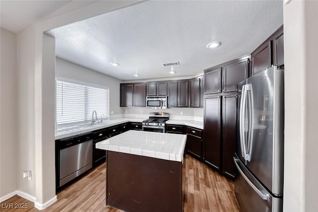 2103 Falcon Crest Ave, North Las Vegas, NV 89031 - kitchen featuring appliances with stainless steel finishes, tile counters, light wood-style floors, a sink, and a kitchen island