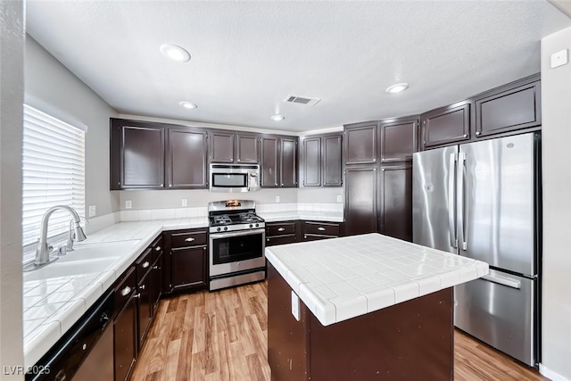 2103 Falcon Crest Ave, North Las Vegas, NV 89031 - kitchen featuring appliances with stainless steel finishes, tile counters, a sink, light wood-type flooring, and recessed lighting