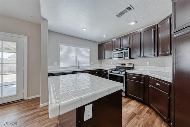 2103 Falcon Crest Ave, North Las Vegas, NV 89031 - kitchen with appliances with stainless steel finishes, plenty of natural light, tile countertops, light wood-style floors, and a textured ceiling
