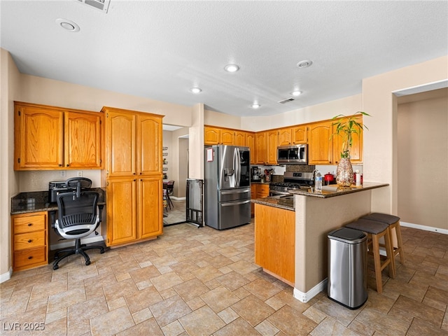 10612 Gum Tree Ct, Las Vegas, NV 89144 - kitchen with appliances with stainless steel finishes, a peninsula, stone finish floors, baseboards, and brown cabinets
