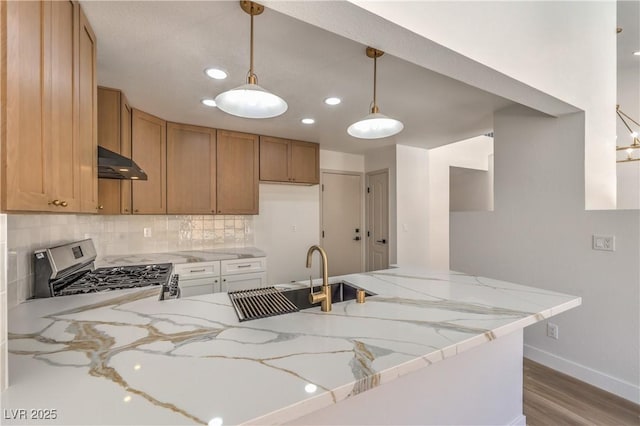 2117 Desert Peak Rd, Las Vegas, NV 89134 - kitchen with under cabinet range hood, gas stove, a peninsula, tasteful backsplash, and light stone counters
