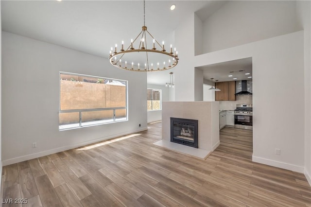 2117 Desert Peak Rd, Las Vegas, NV 89134 - unfurnished living room featuring a chandelier, light wood-type flooring, baseboards, a high ceiling, and a fireplace with flush hearth