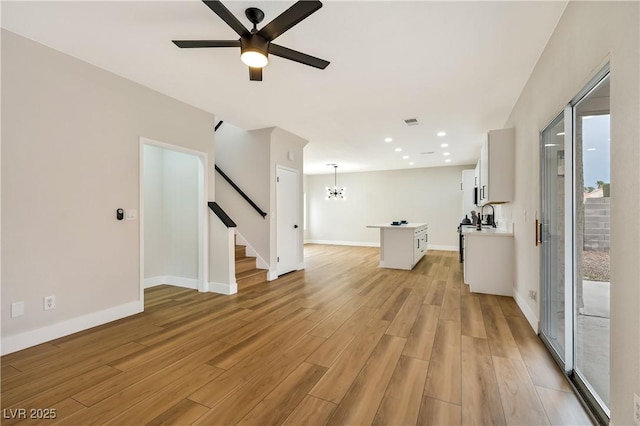 6388 Canyon Dawn Ave, Las Vegas, NV 89108 - unfurnished living room with stairs, ceiling fan, a chandelier, light wood finished floors, and baseboards