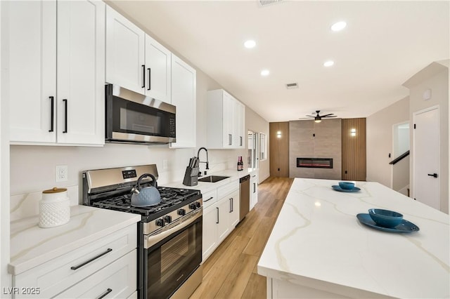 6388 Canyon Dawn Ave, Las Vegas, NV 89108 - kitchen with stainless steel appliances, ceiling fan, light wood-style floors, a tiled fireplace, and white cabinetry
