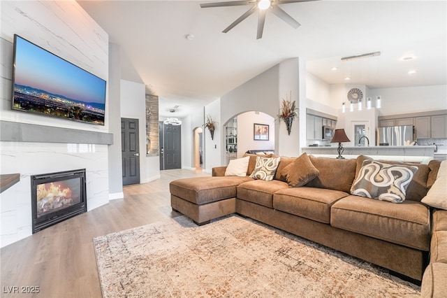 2144 Paganini Ave, Henderson, NV 89052 - living room featuring a ceiling fan, arched walkways, light wood-style flooring, a fireplace, and baseboards