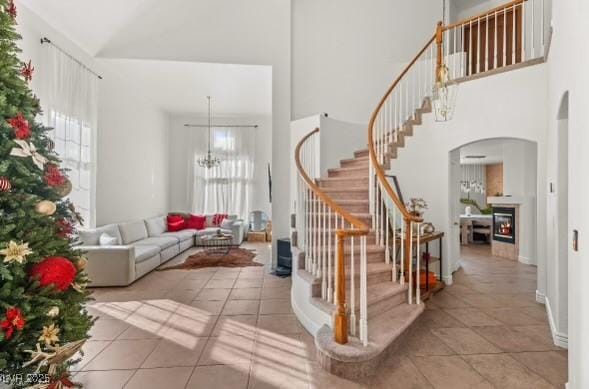 59 Desert Dawn Ln, Henderson, NV 89074 - stairway featuring arched walkways, a high ceiling, tile patterned floors, a glass covered fireplace, and a chandelier