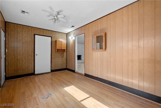 5101 Churchill Ave, Las Vegas, NV 89107 - unfurnished bedroom featuring light wood-style floors, wooden walls, a textured ceiling, and a ceiling fan