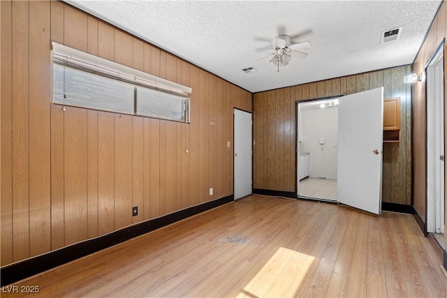 5101 Churchill Ave, Las Vegas, NV 89107 - unfurnished bedroom with light wood-style floors, a textured ceiling, wood walls, and a ceiling fan