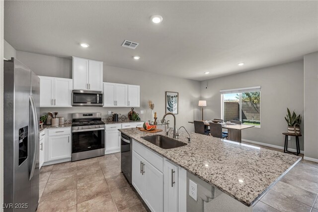 9876 Magnus Ct, Las Vegas, NV 89178 - kitchen featuring stainless steel appliances, a sink, a center island with sink, white cabinets, and light stone countertops