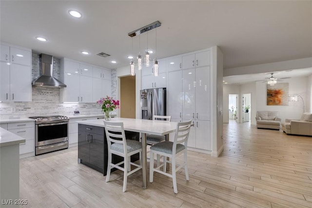 8221 Bay Dunes St, Las Vegas, NV 89131 - kitchen with stainless steel appliances, wall chimney exhaust hood, a kitchen bar, modern cabinets, and light wood-style flooring