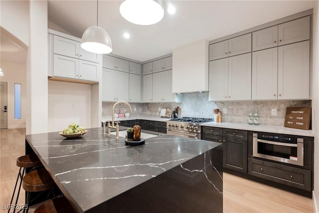 8104 Bay Harbor Dr, Las Vegas, NV 89128 - kitchen with stainless steel appliances, light wood-style floors, dark stone counters, backsplash, and decorative light fixtures