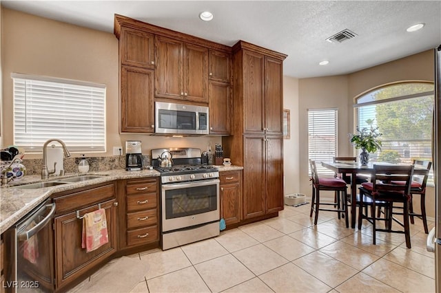 805 Palmero Way, Boulder City, NV 89005 - kitchen featuring appliances with stainless steel finishes, a sink, brown cabinetry, light tile patterned floors, and light stone countertops