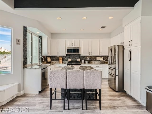 9718 Camino Capistrano Ln, Las Vegas, NV 89147 - kitchen with stainless steel appliances, a sink, white cabinets, tasteful backsplash, and light wood-type flooring