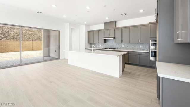 362 Tigullio Ave, Henderson, NV 89011 - kitchen featuring gray cabinetry, backsplash, double oven, under cabinet range hood, and light wood-type flooring