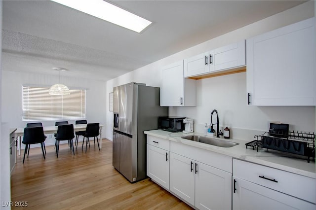 6301 Garwood Ave, Las Vegas, NV 89107 - kitchen featuring a sink, black microwave, white cabinetry, light wood-style flooring, and pendant lighting