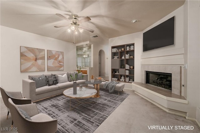 2104 Inverness Dr, Henderson, NV 89074 - living room with ceiling fan, arched walkways, a tiled fireplace, built in shelves, and carpet flooring