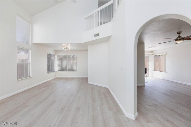 92 Sea Holly Way, Henderson, NV 89074 - unfurnished living room featuring plenty of natural light, arched walkways, a ceiling fan, wood finished floors, and a high ceiling