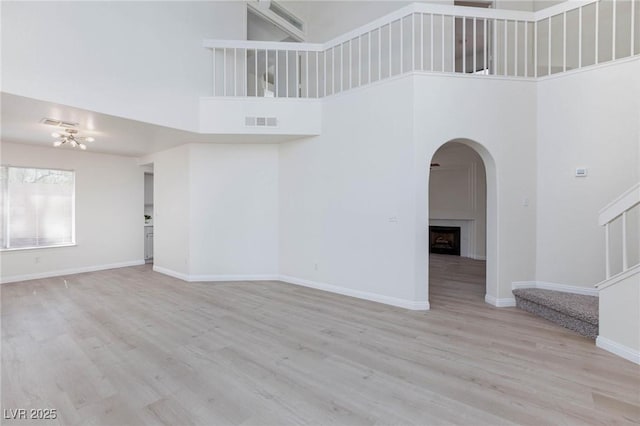 92 Sea Holly Way, Henderson, NV 89074 - unfurnished living room featuring a high ceiling, stairs, wood finished floors, arched walkways, and a large fireplace