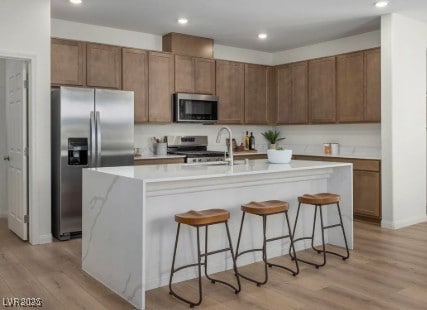739 Wild Highlands Ln, Henderson, NV 89015 - kitchen with stainless steel appliances, light countertops, light wood-style floors, a kitchen breakfast bar, and a center island with sink
