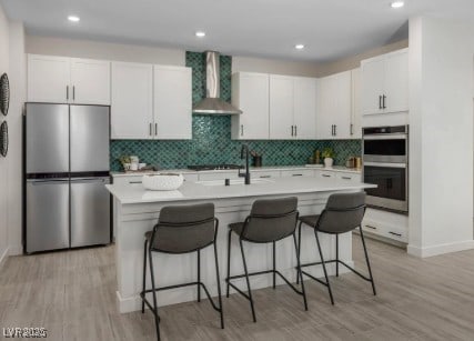 737 Wild Highlands Ln, Henderson, NV 89015 - kitchen with stainless steel appliances, wall chimney exhaust hood, decorative backsplash, a center island with sink, and a kitchen bar