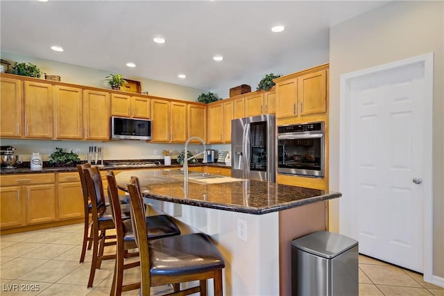 6440 Bristlebird St, North Las Vegas, NV 89084 - kitchen with appliances with stainless steel finishes, light tile patterned floors, dark stone counters, a breakfast bar, and an island with sink