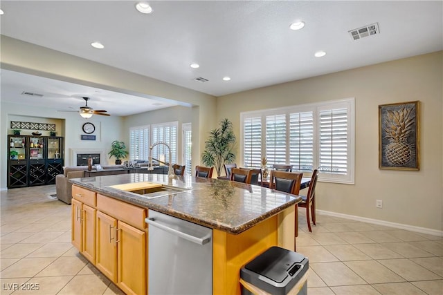6440 Bristlebird St, North Las Vegas, NV 89084 - kitchen with dishwasher, a glass covered fireplace, light tile patterned floors, an island with sink, and a ceiling fan