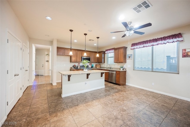 132 Soaring Sky Ave, Henderson, NV 89011 - kitchen featuring appliances with stainless steel finishes, brown cabinetry, a kitchen island, ceiling fan, and a kitchen bar