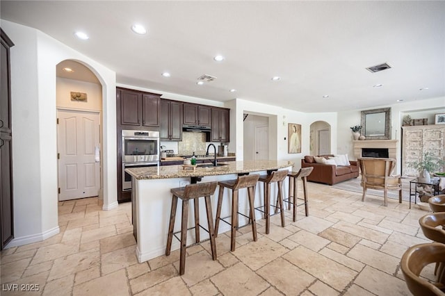 7538 Mustang St, Las Vegas, NV 89131 - kitchen with stainless steel double oven, stone tile flooring, open floor plan, dark brown cabinets, and a kitchen breakfast bar