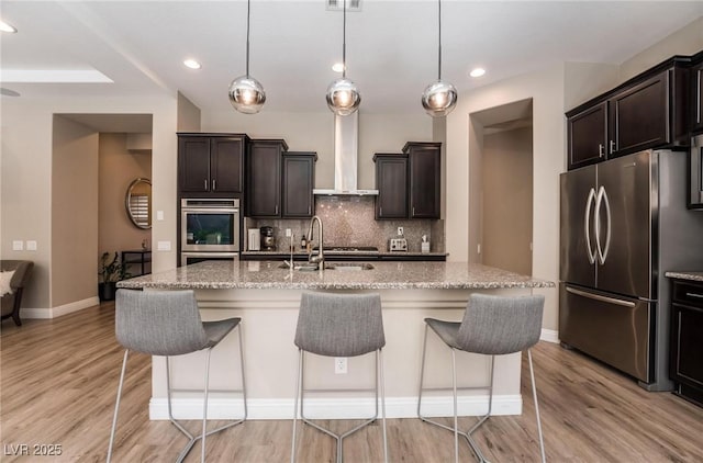2896 Grande Arch St, Henderson, NV 89044 - kitchen featuring appliances with stainless steel finishes, wall chimney range hood, light wood finished floors, decorative backsplash, and recessed lighting