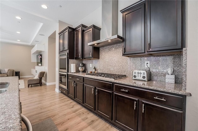 2896 Grande Arch St, Henderson, NV 89044 - kitchen with wall chimney exhaust hood, appliances with stainless steel finishes, open floor plan, backsplash, and light wood-type flooring