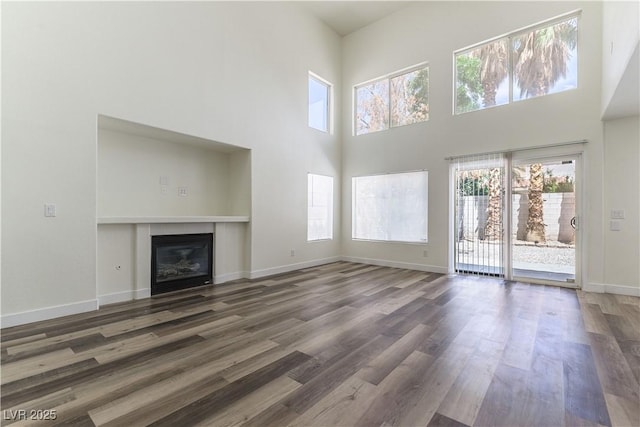 10162 Lemon Thyme St, Las Vegas, NV 89183 - unfurnished living room featuring a towering ceiling, wood finished floors, a glass covered fireplace, and baseboards