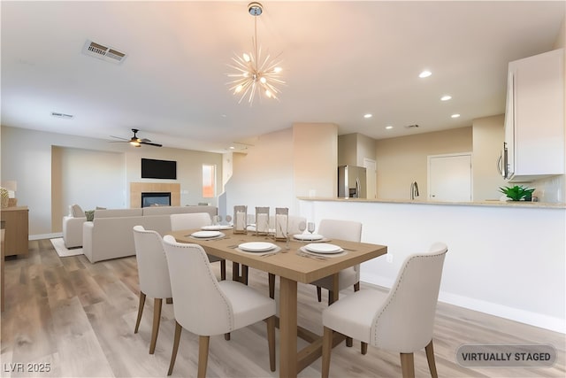 1512 Groom Ave, North Las Vegas, NV 89081 - dining room featuring a tiled fireplace, light wood-style floors, baseboards, ceiling fan, and a chandelier